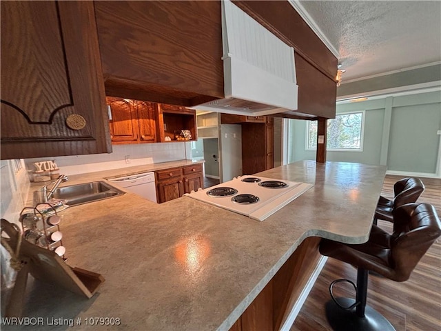 kitchen with a breakfast bar, custom range hood, a sink, a textured ceiling, and white appliances