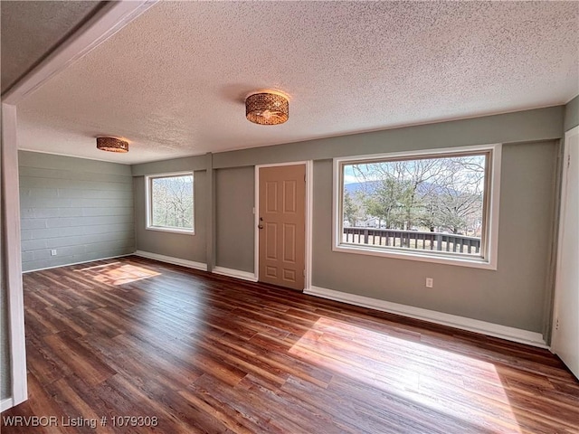 spare room featuring a textured ceiling, wood finished floors, and baseboards