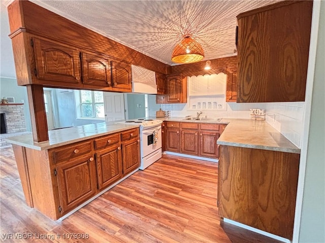 kitchen featuring white range with electric stovetop, light wood-style floors, a sink, wall chimney range hood, and a peninsula