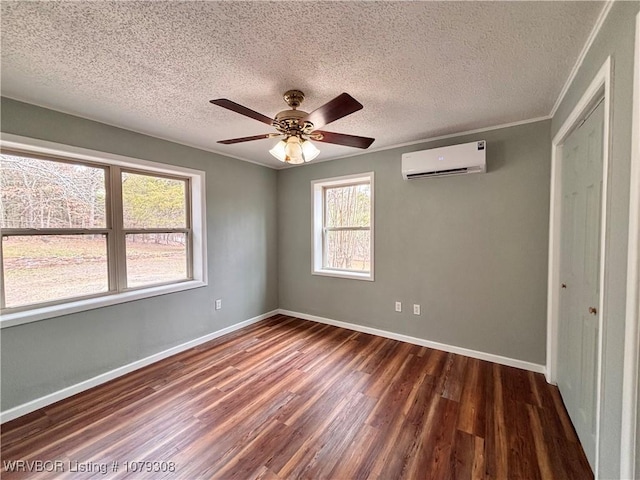 spare room featuring an AC wall unit, a textured ceiling, baseboards, and wood finished floors