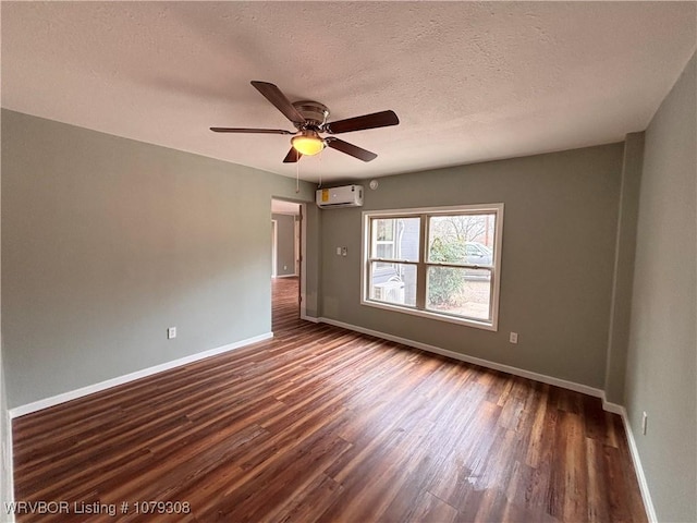 unfurnished room with a textured ceiling, a wall unit AC, dark wood finished floors, and baseboards