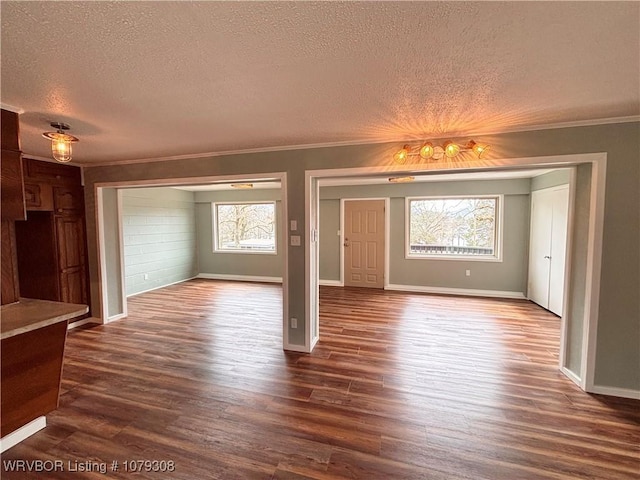 unfurnished living room featuring dark wood-style floors, ornamental molding, a textured ceiling, and baseboards