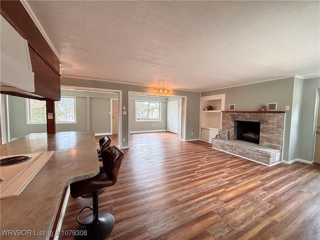 unfurnished living room featuring a textured ceiling, built in shelves, wood finished floors, a brick fireplace, and crown molding