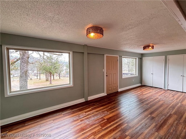 unfurnished bedroom featuring multiple closets, a textured ceiling, baseboards, and wood finished floors