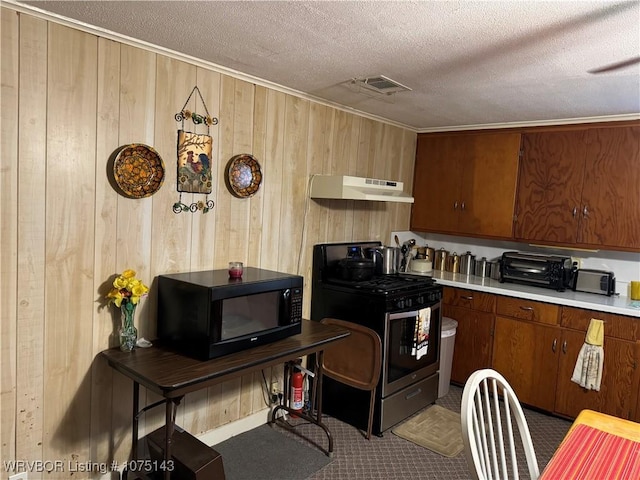 kitchen with a textured ceiling, wooden walls, and stainless steel range oven