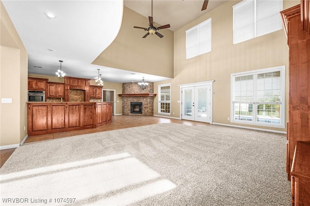 unfurnished living room with french doors, ceiling fan with notable chandelier, a stone fireplace, a towering ceiling, and light colored carpet