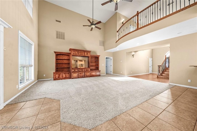 unfurnished living room featuring light carpet, a towering ceiling, and ceiling fan