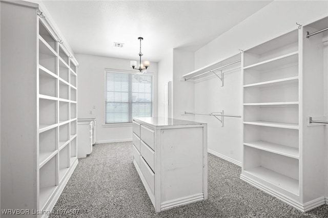 spacious closet with dark colored carpet and a chandelier