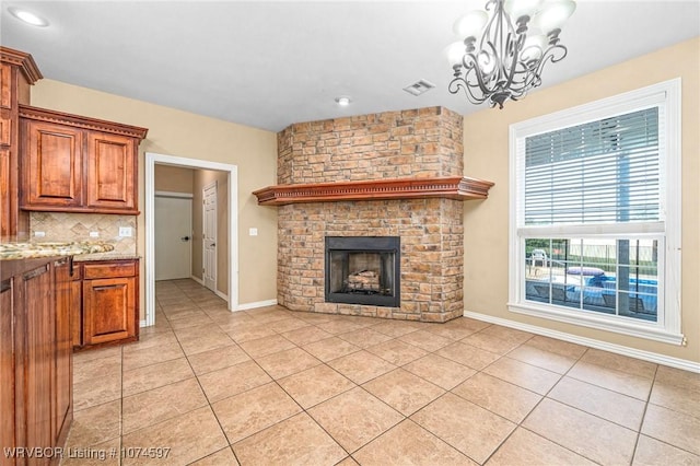 kitchen with decorative backsplash, light stone counters, a large fireplace, a notable chandelier, and hanging light fixtures