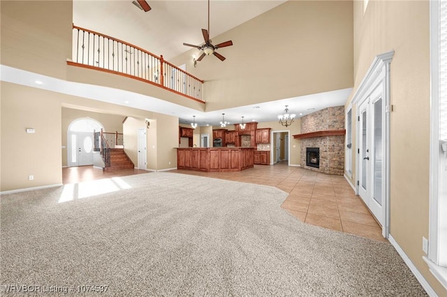 unfurnished living room with light carpet, a high ceiling, ceiling fan with notable chandelier, and a stone fireplace