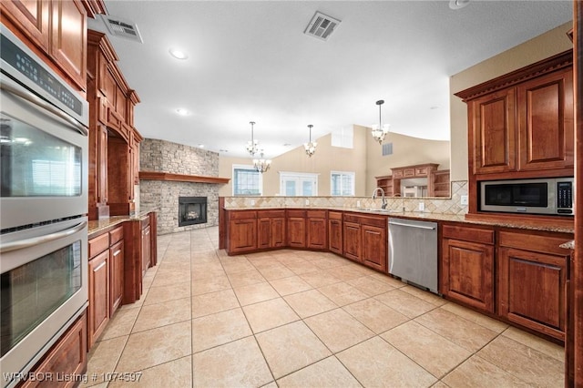 kitchen featuring sink, stainless steel appliances, an inviting chandelier, a stone fireplace, and decorative light fixtures