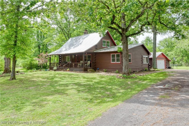 log-style house featuring driveway, a chimney, an outbuilding, a front yard, and a porch