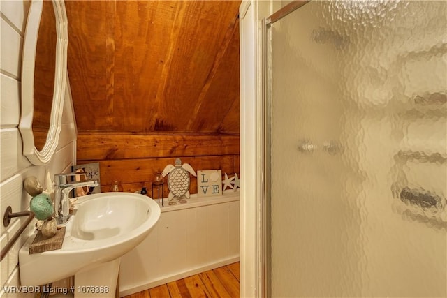 bathroom featuring a shower with shower door, sink, wood walls, and hardwood / wood-style floors