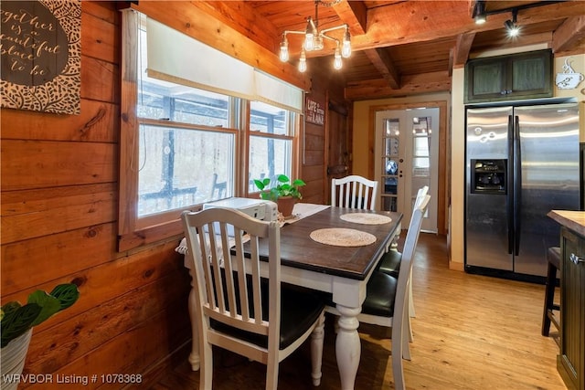 dining area featuring a chandelier, light wood-style floors, wooden ceiling, wood walls, and beam ceiling