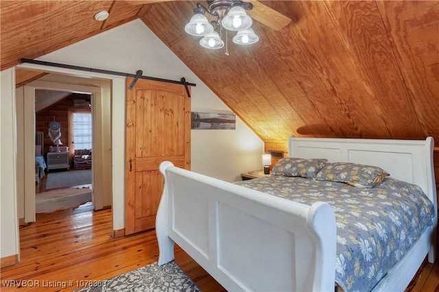 bedroom with lofted ceiling, wood ceiling, light wood-type flooring, ceiling fan, and a barn door