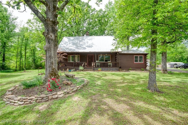 view of front of property with covered porch, a chimney, a front yard, and log siding