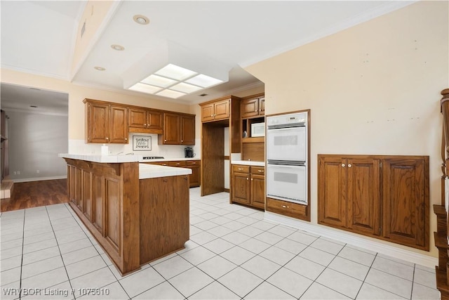 kitchen featuring kitchen peninsula, light tile patterned floors, white appliances, and crown molding