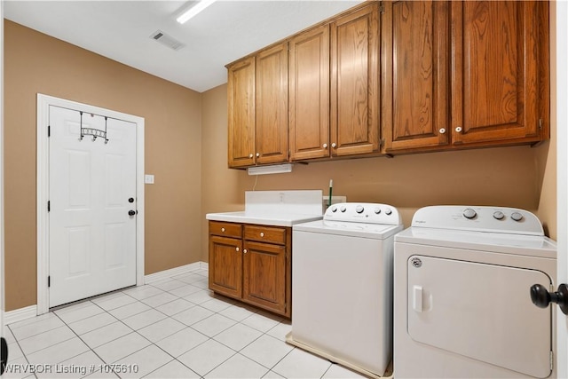 clothes washing area featuring cabinets, light tile patterned floors, and washing machine and dryer