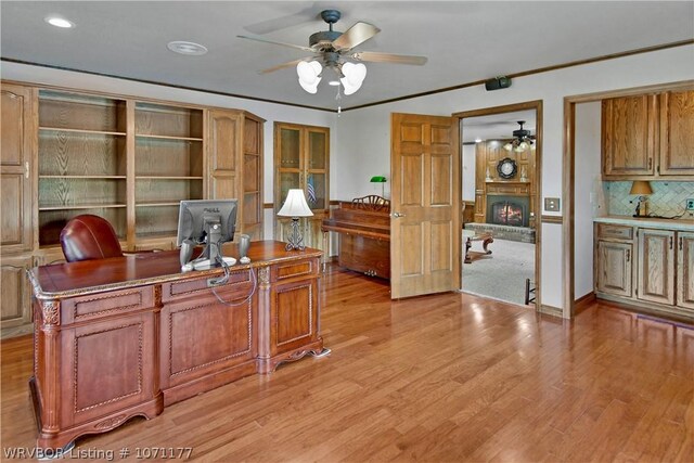 office area with ceiling fan, ornamental molding, a fireplace, and light hardwood / wood-style flooring