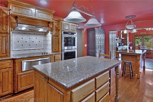 kitchen with decorative light fixtures, extractor fan, double oven, and a kitchen island