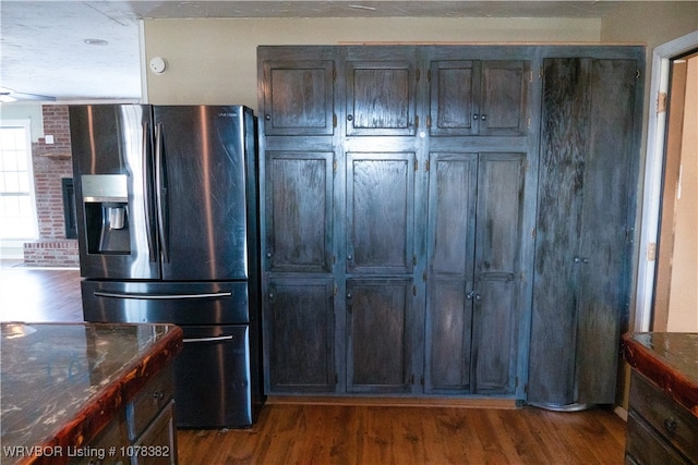 kitchen with dark wood-type flooring, stainless steel fridge, and dark stone countertops