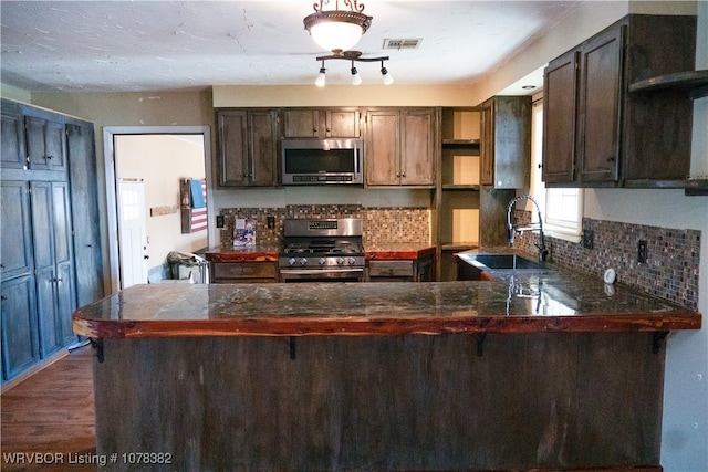 kitchen with appliances with stainless steel finishes, kitchen peninsula, sink, dark brown cabinets, and tasteful backsplash