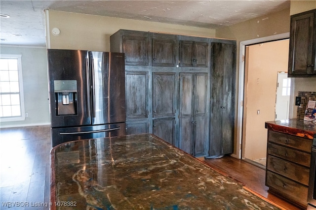 kitchen featuring dark wood-type flooring, dark stone countertops, stainless steel fridge with ice dispenser, and dark brown cabinets