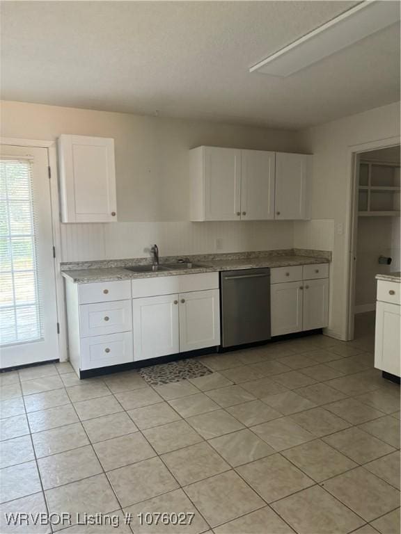 kitchen with stainless steel dishwasher, white cabinets, light tile patterned floors, and sink