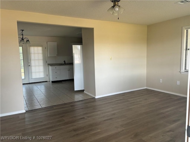 empty room with a textured ceiling, dark hardwood / wood-style flooring, and ceiling fan with notable chandelier