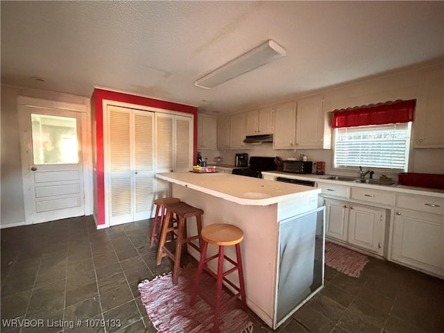 kitchen with a breakfast bar area, stove, a kitchen island, white cabinetry, and light countertops