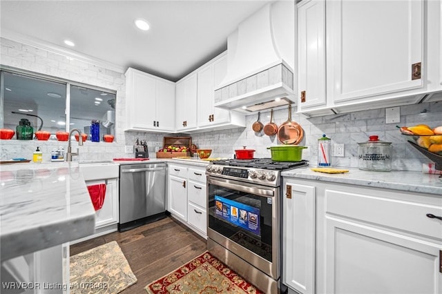 kitchen featuring appliances with stainless steel finishes, custom exhaust hood, white cabinetry, sink, and light stone counters