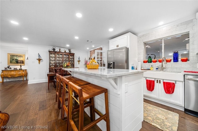 kitchen with white cabinets, a kitchen island, sink, a breakfast bar, and stainless steel appliances