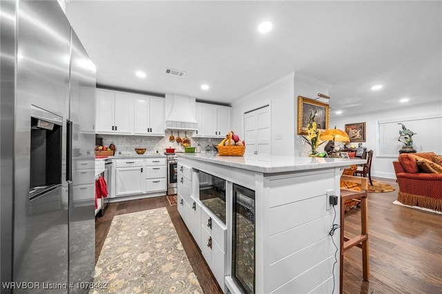 kitchen featuring white cabinetry, appliances with stainless steel finishes, custom range hood, and a kitchen island