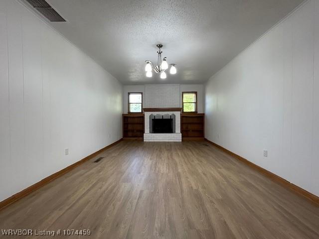 unfurnished living room with a fireplace, hardwood / wood-style floors, a textured ceiling, and a notable chandelier