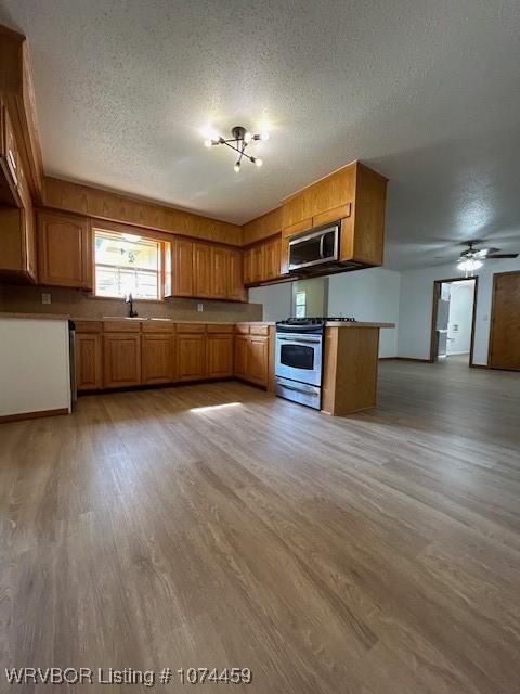 kitchen with a textured ceiling, stainless steel appliances, light hardwood / wood-style flooring, and sink