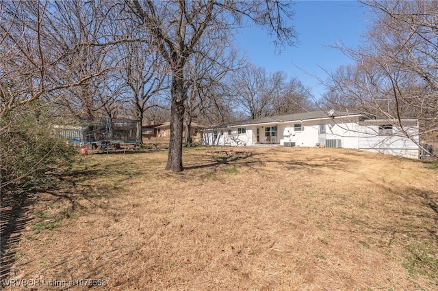 back of house with a yard, central AC unit, and a trampoline