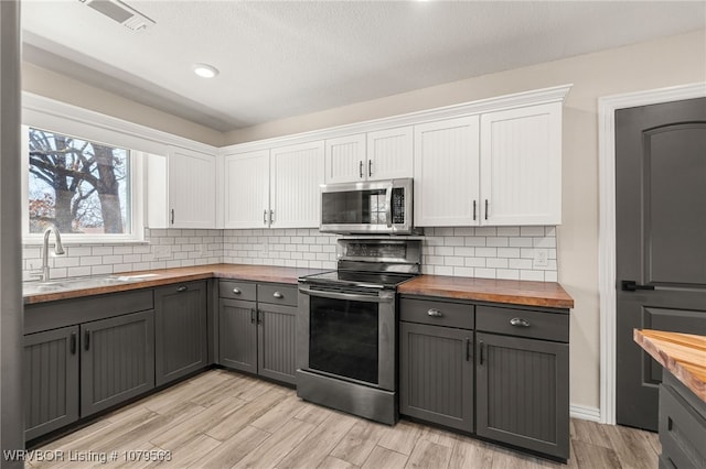 kitchen featuring a sink, gray cabinetry, stainless steel appliances, butcher block countertops, and white cabinetry