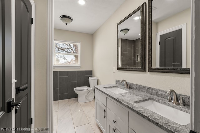 full bathroom featuring a sink, marble finish floor, toilet, and tile walls