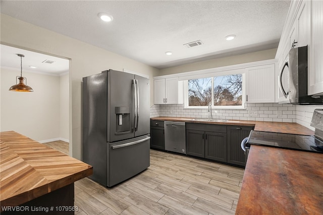 kitchen with visible vents, a sink, stainless steel appliances, white cabinets, and wooden counters