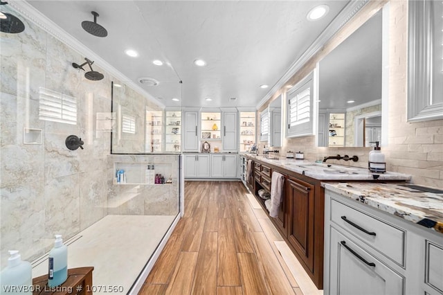 bathroom with vanity, wood-type flooring, ornamental molding, and tiled shower