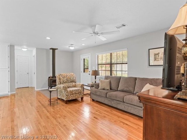 living room featuring a wood stove, ceiling fan, and light hardwood / wood-style floors