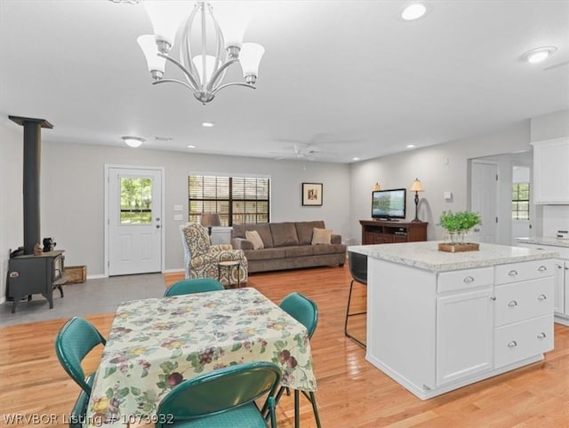 kitchen with a wood stove, white cabinetry, decorative light fixtures, a kitchen island, and ceiling fan with notable chandelier