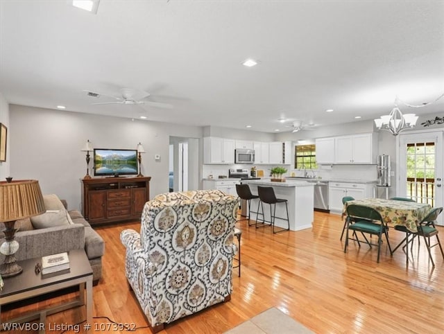 living room with ceiling fan with notable chandelier and light hardwood / wood-style floors