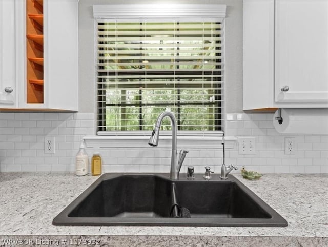 kitchen with tasteful backsplash, light stone counters, sink, and white cabinets