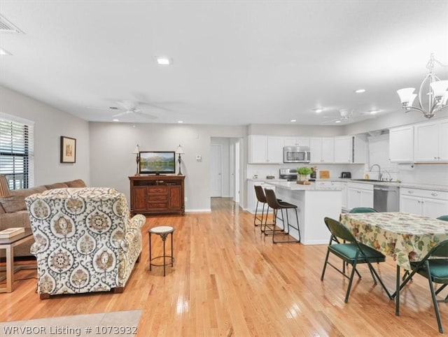 interior space featuring ceiling fan with notable chandelier, light hardwood / wood-style flooring, and sink