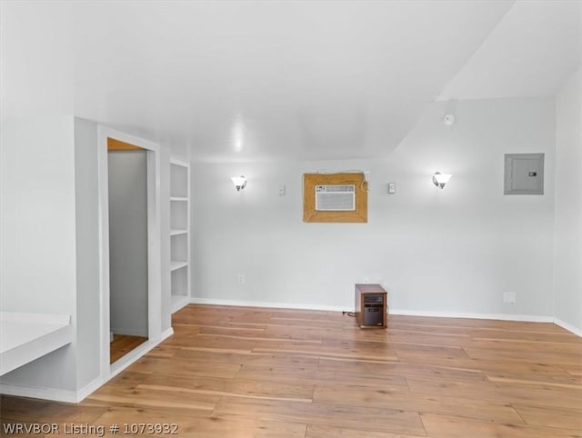 empty room featuring electric panel, built in features, light hardwood / wood-style floors, and a wall mounted air conditioner