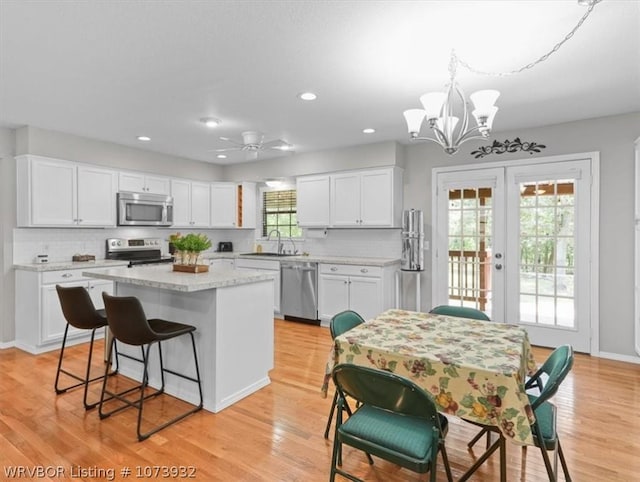 kitchen with ceiling fan with notable chandelier, stainless steel appliances, pendant lighting, white cabinets, and a kitchen island