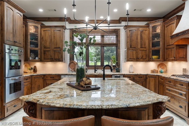 kitchen with backsplash, stainless steel appliances, premium range hood, and an island with sink