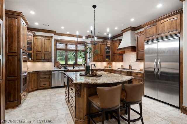 kitchen featuring a kitchen island with sink, stainless steel appliances, crown molding, decorative backsplash, and custom range hood