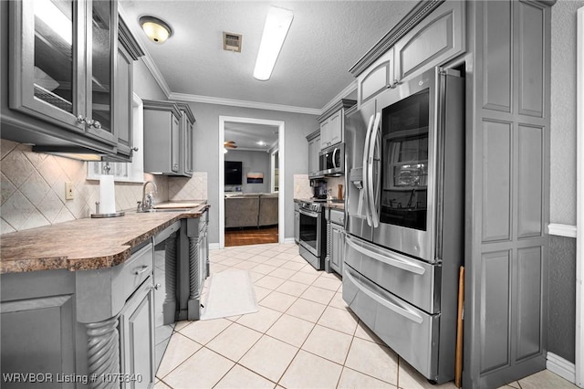 kitchen with gray cabinetry, sink, a textured ceiling, appliances with stainless steel finishes, and ornamental molding